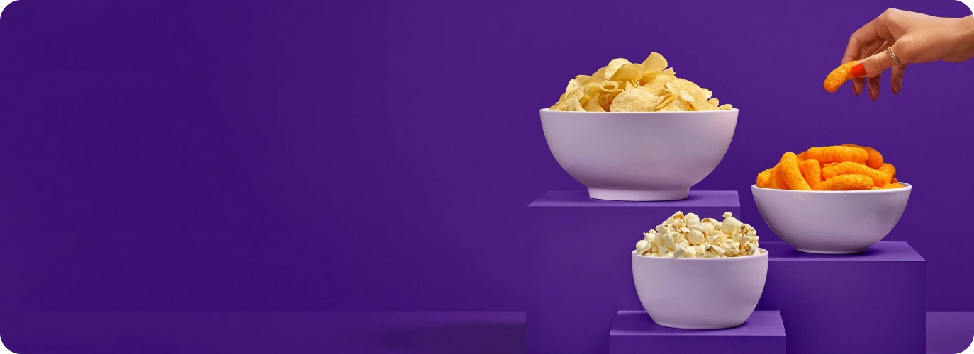 Potato chips, cheese puffs, and popcorn are displayed in bowls on a tiered purple display