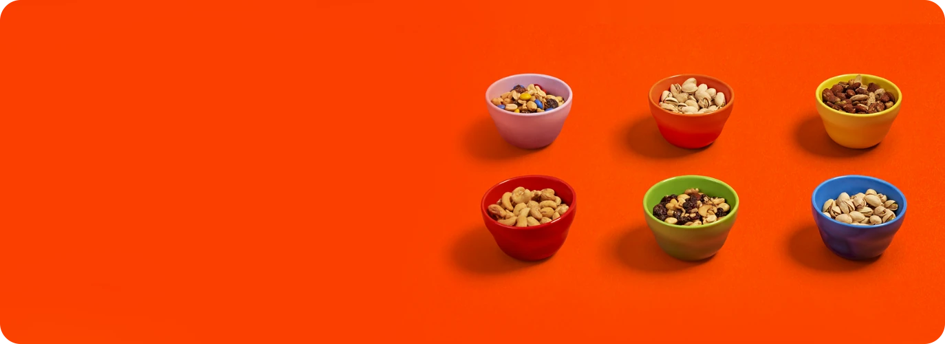 Cashews, pistaccios, and mixed nuts are displayed in colorful bowls against an orange surface